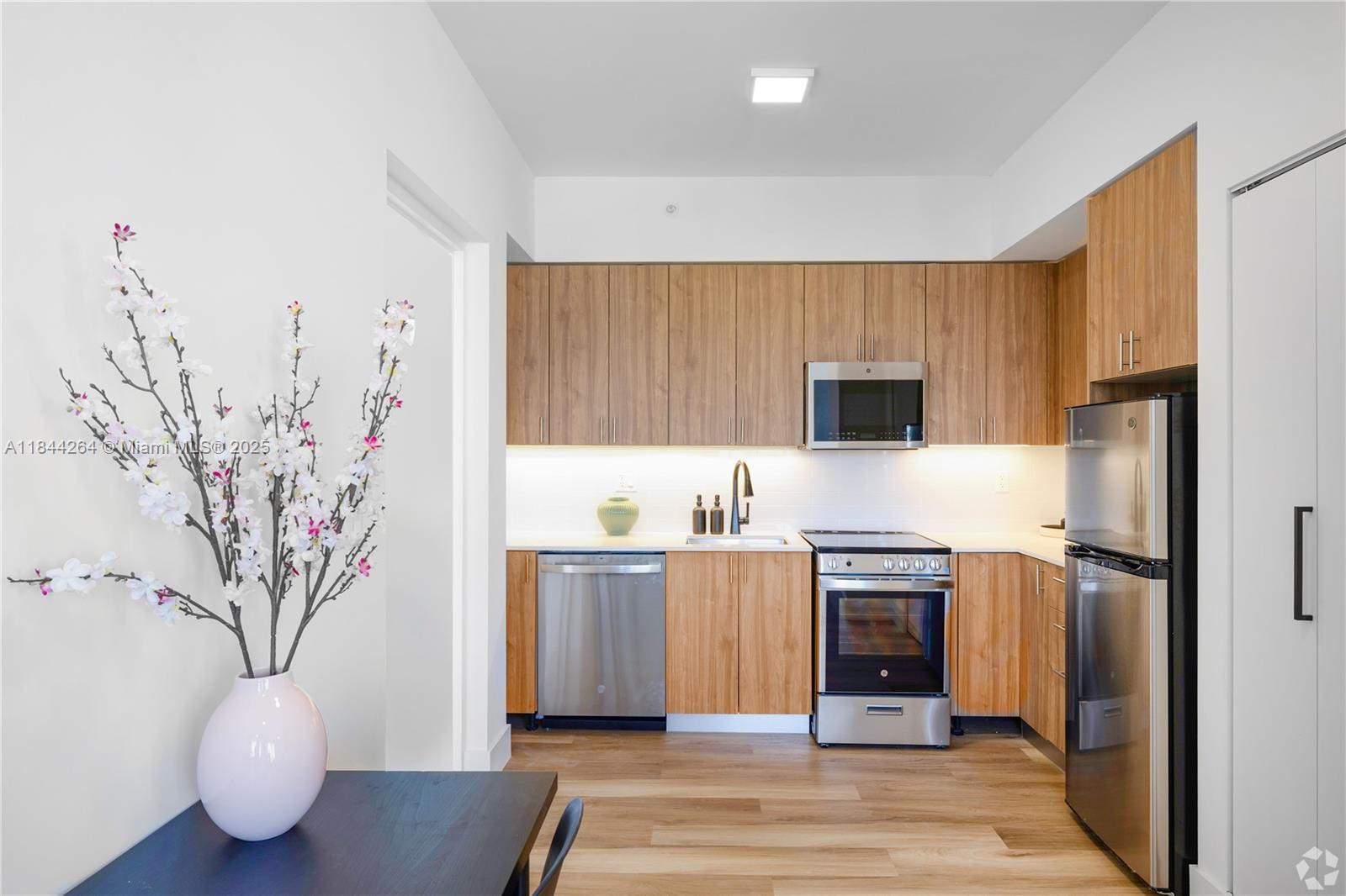 650 Southwest 1st Street, Unit 203 Miami, FL 33130 - Photo 2 of 15 a kitchen with stainless steel appliances a white refrigerator a stove a sink and white cabinets with wooden floor