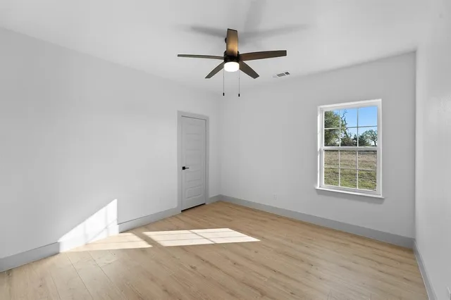 an empty room with wooden floor fan and windows