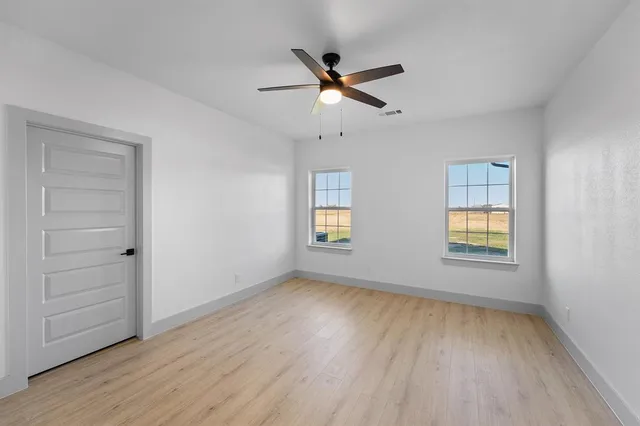 a view of empty room with wooden floor and fan
