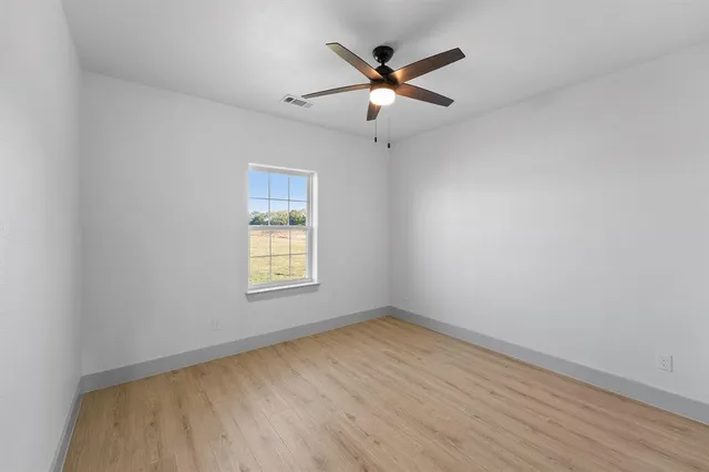 a view of an empty room and kitchen with wooden floor