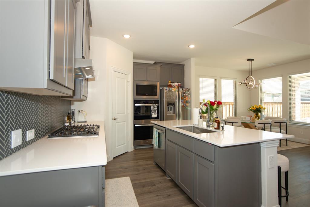 3813 Oldham Road Little Elm, TX 75068 - Photo 9 of 27 Kitchen featuring gray cabinetry, dark wood-style flooring, stainless steel appliances, a breakfast bar area, and light stone counters