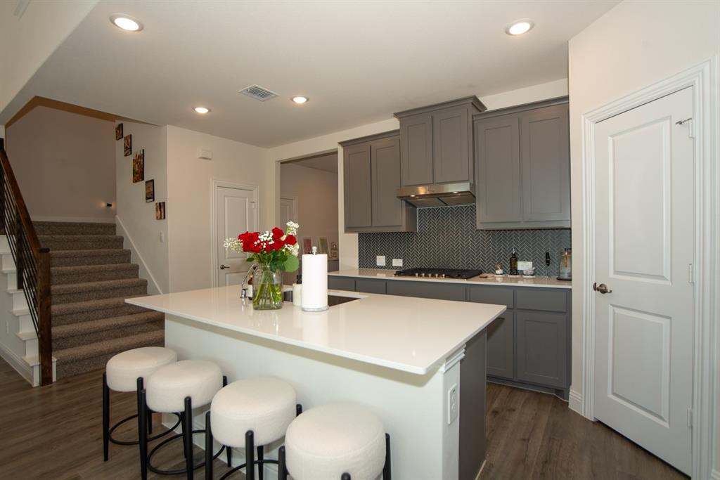 3813 Oldham Road Little Elm, TX 75068 - Photo 10 of 27 Kitchen featuring a kitchen breakfast bar, dark wood-style flooring, an island with sink, gray cabinetry, and decorative backsplash