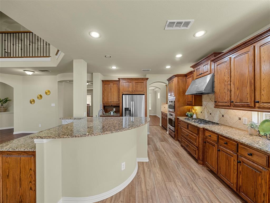 5143 Stream Crest Way Fairview, TX 75069 - Photo 11 of 35 Kitchen with arched walkways, wood finish cabinets, light wood finished floors, light stone countertops, and a large island