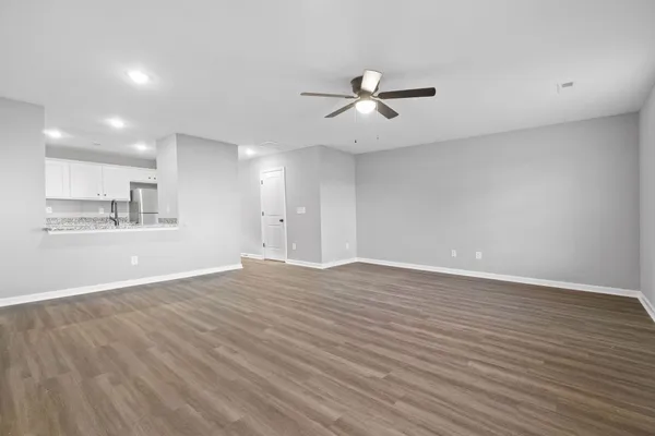 a view of an empty room with wooden floor and a kitchen