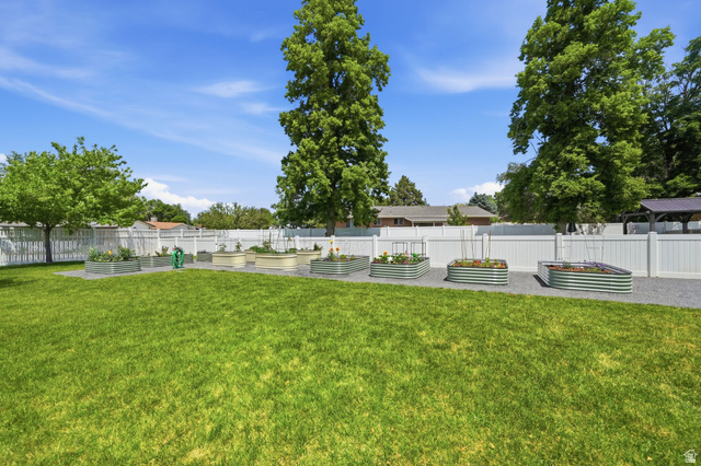 6969 South 855 East Midvale, UT 84047 - Photo 55 of 55 Expansive backyard featuring a manicured lawn, a white privacy fence, and multiple raised garden beds set on a gravel path