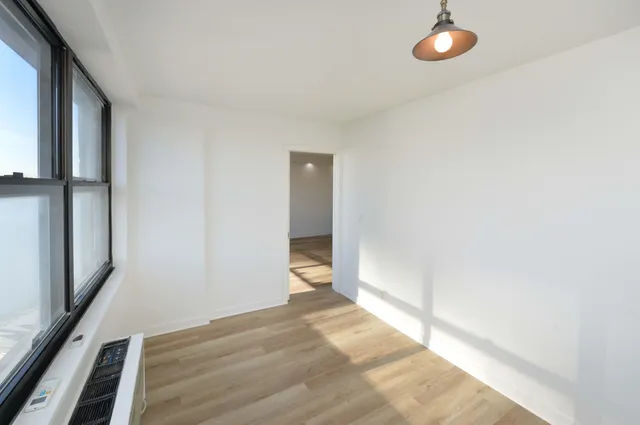 a view of an empty room with wooden floor and a window
