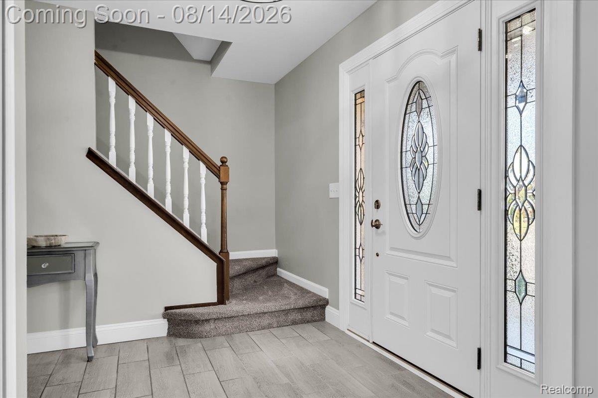 47321 Susan Road Macomb, MI 48044 - Photo 5 of 46 Wood-finish flooring, decorative glass entry door, staircase with wood handrail, paneled door, and carpeted stairs