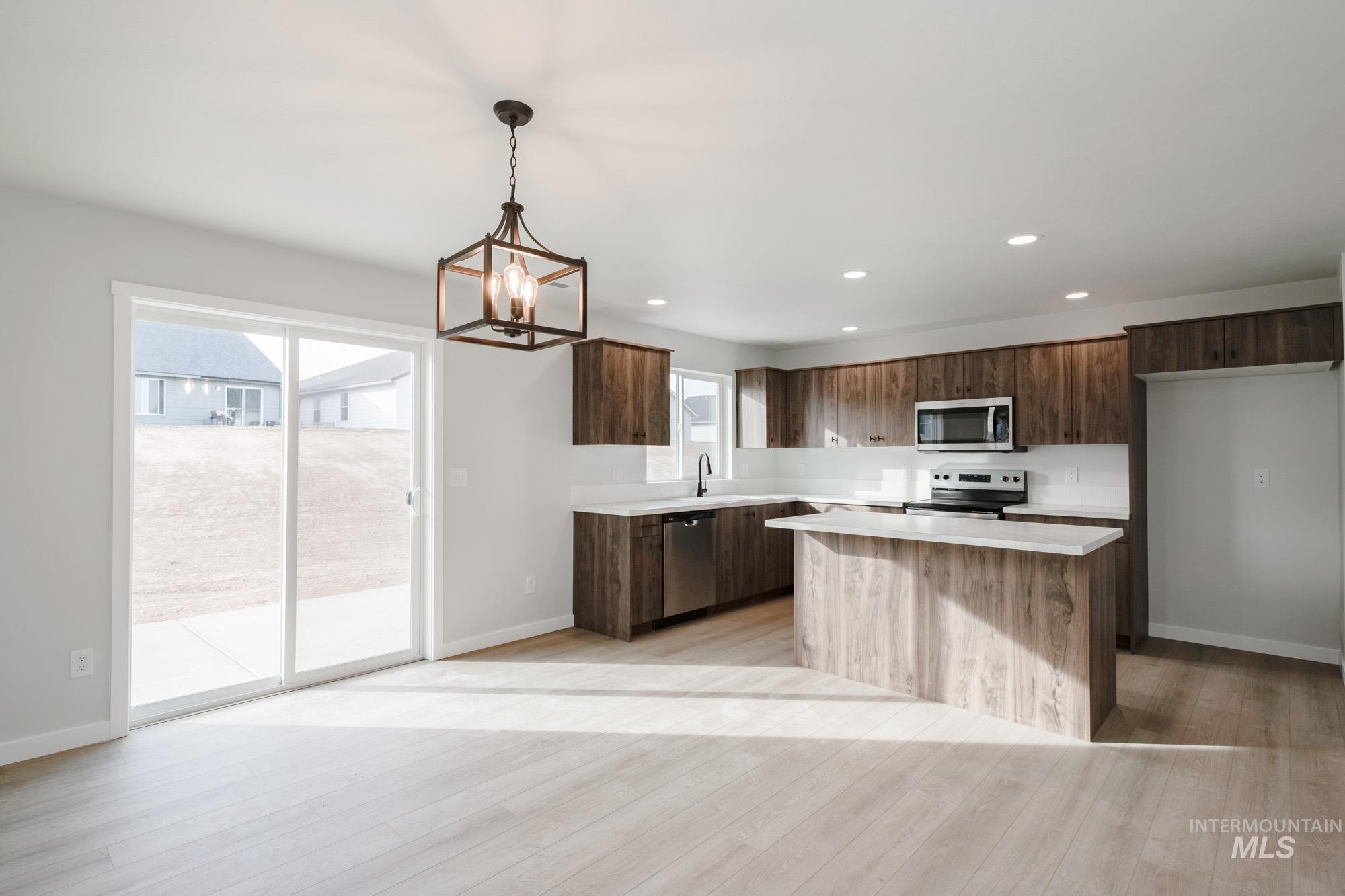 13697 Inman Court Caldwell, ID 83607 - Photo 8 of 23 Kitchen with a kitchen island, stainless steel appliances, dark wood finish cabinets, suspended lighting, and light wood finished floors