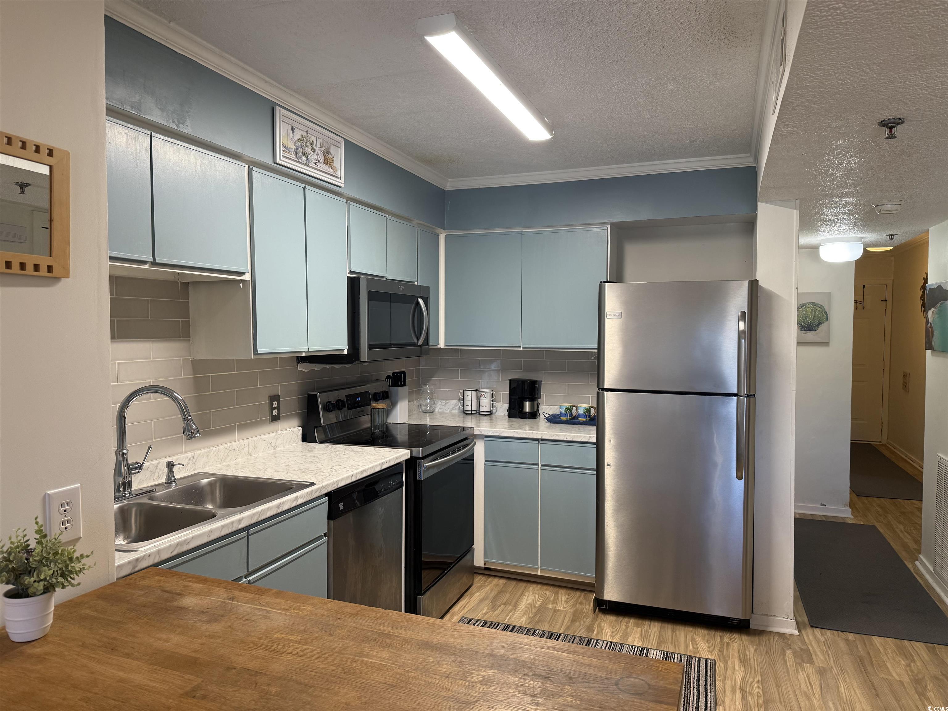 4350 Intercoastal Drive, Unit INTERCOASTAL VILLAGE UNI Little River, SC 29566 - Photo 20 of 21 Kitchen featuring appliances with stainless steel finishes, tasteful backsplash, light countertops, crown molding, and light wood-type flooring