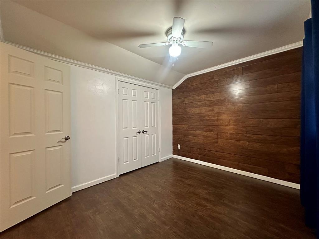 2734 Mildred Street Waco, TX 76706 - Photo 23 of 32 Upstairs bedroom featuring wooden walls, lofted ceiling, dark wood-type flooring, a ceiling fan, and a closet