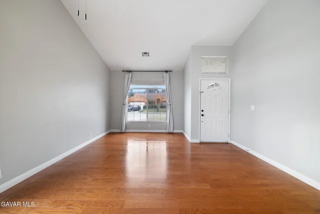 a view of an empty room with wooden floor and a window