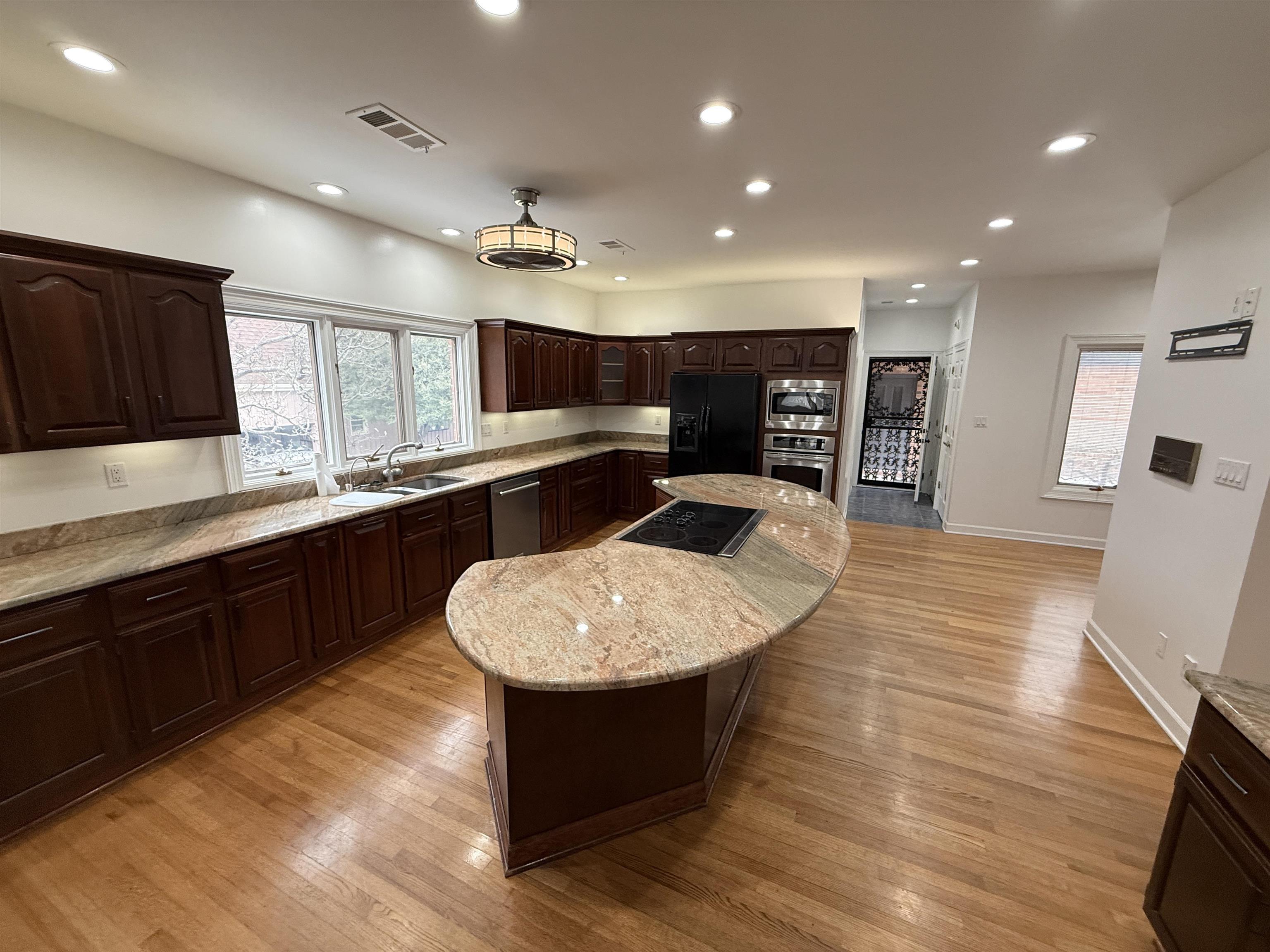 765 Sweetbrier Road Memphis, TN 38120 - Photo 7 of 33 Kitchen with dark wood finish cabinets, a center island, light wood-style floors, black appliances, and light stone countertops