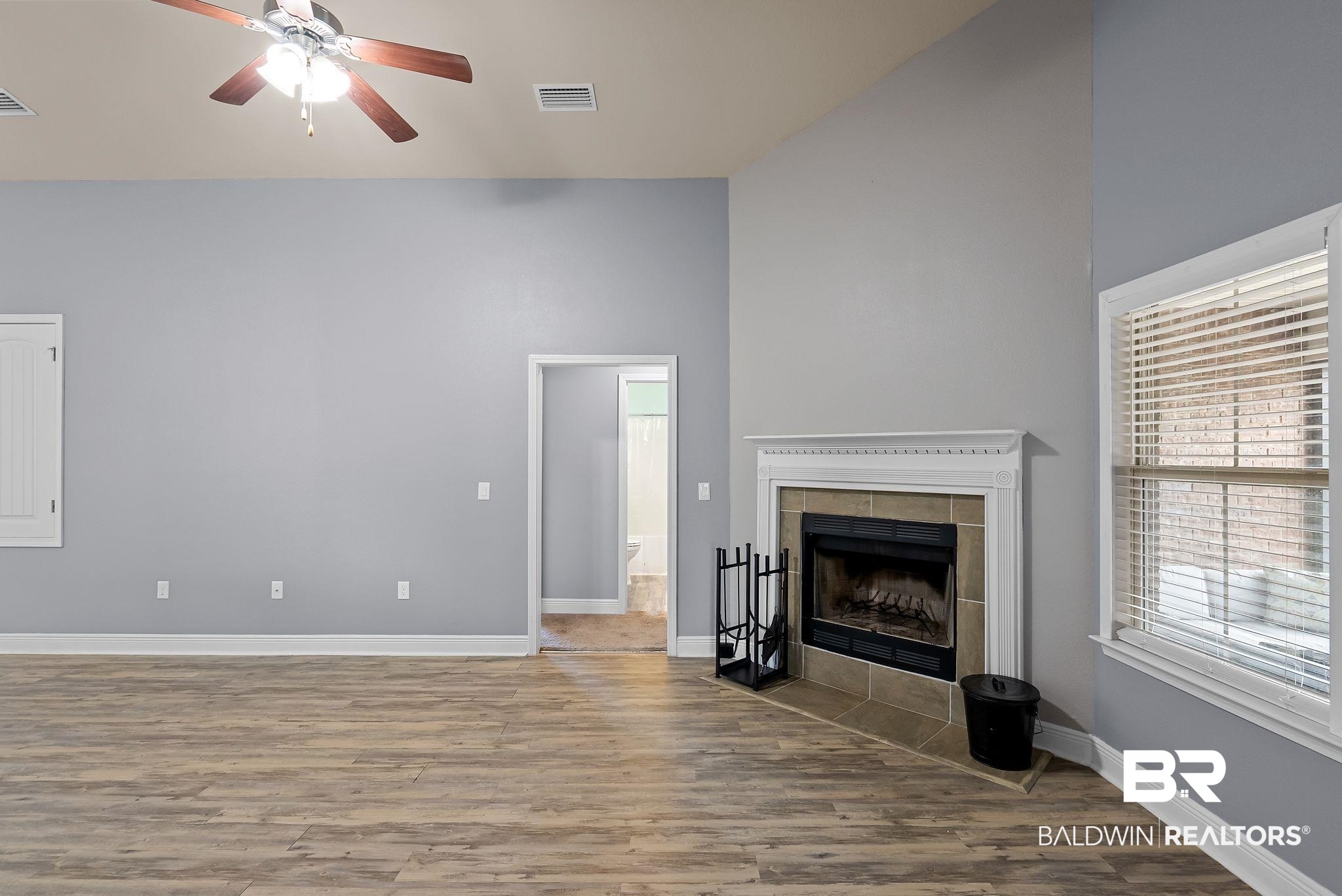 22076 Garland Loop Silverhill, AL 36576 - Photo 4 of 27 Living area featuring wood-finish flooring, a corner fireplace with a tiled hearth and decorative mantel, vaulted ceilings, and a ceiling fan