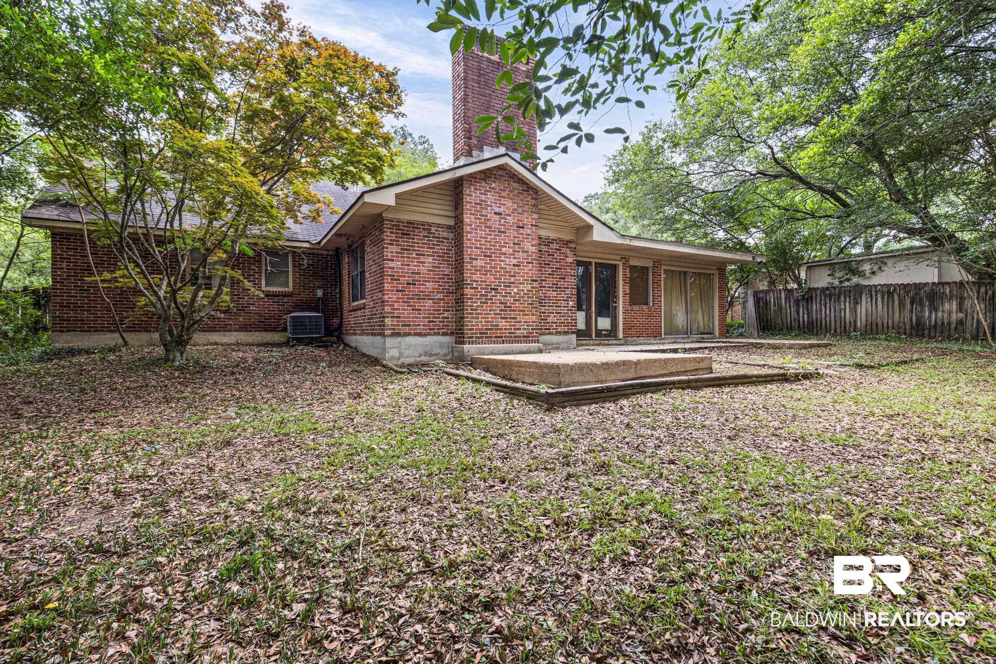 5510 Richmond Road Mobile, AL 36608 - Photo 19 of 21 Brick exterior featuring a prominent chimney, concrete patio area, and mature trees