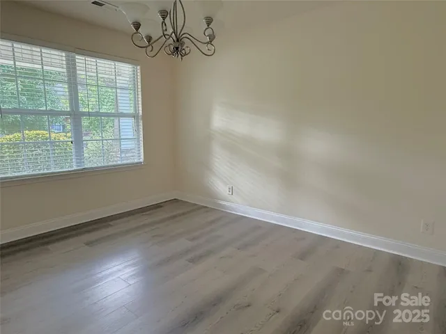 an empty room with wooden floor chandelier and windows