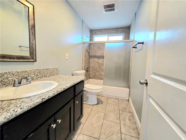 a bathroom with a granite countertop sink a toilet a mirror and shower