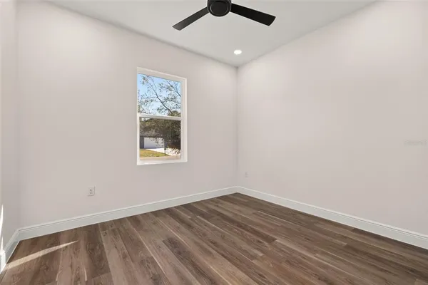 an empty room with wooden floor ceiling fan and window