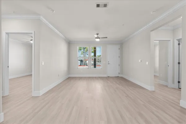 an empty room with wooden floor chandelier fan and windows