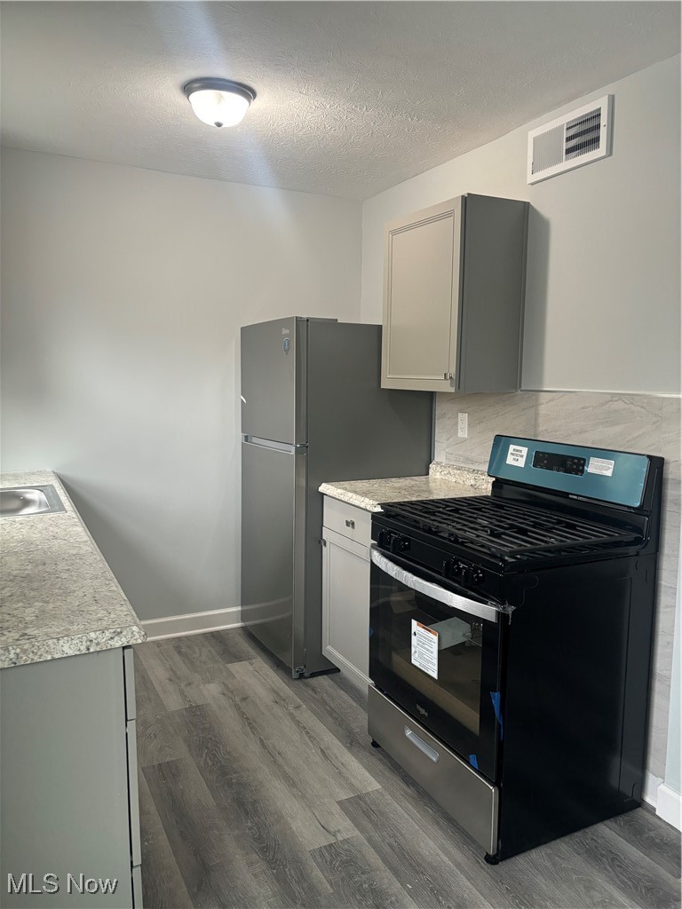 2525 Noble Road, Unit C3 Cleveland Heights, OH 44121 - Photo 2 of 11 Kitchen featuring hardwood / wood-style floors, gray cabinets, a textured ceiling, tasteful backsplash, and stainless steel appliances
