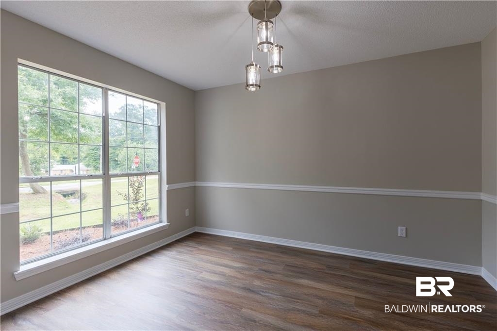 101 Lawson Road Daphne, AL 36526 - Photo 13 of 20 Spacious room featuring a large grid-pattern window, wood-finish flooring, neutral wall tones, white trim, and a contemporary ceiling light fixture