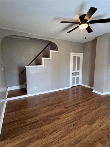 a view of an empty room with wooden floor and a ceiling fan