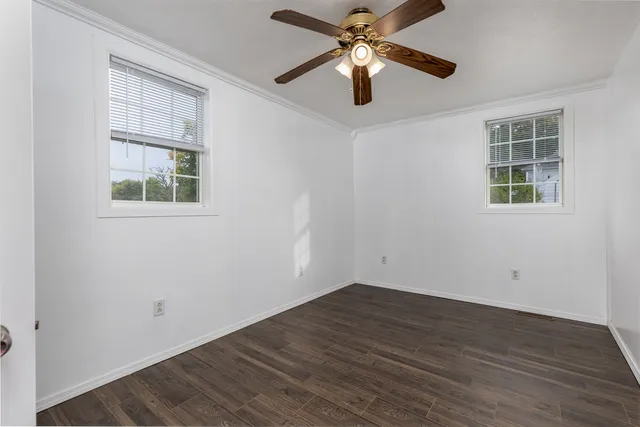 an empty room with wooden floor ceiling fan and windows