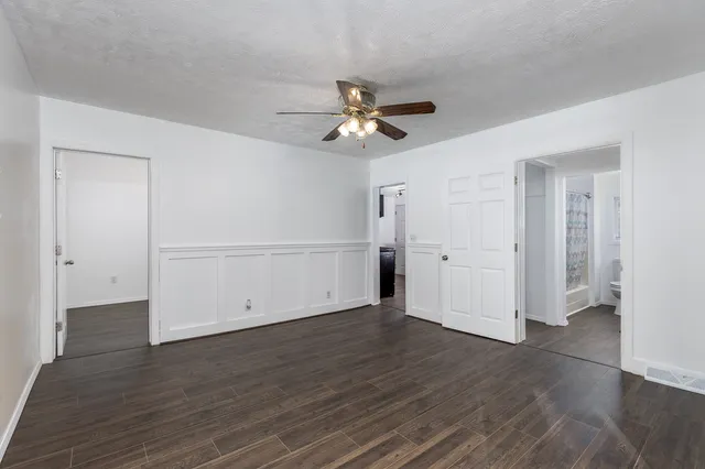 an empty room with wooden floor a ceiling fan white walls and windows