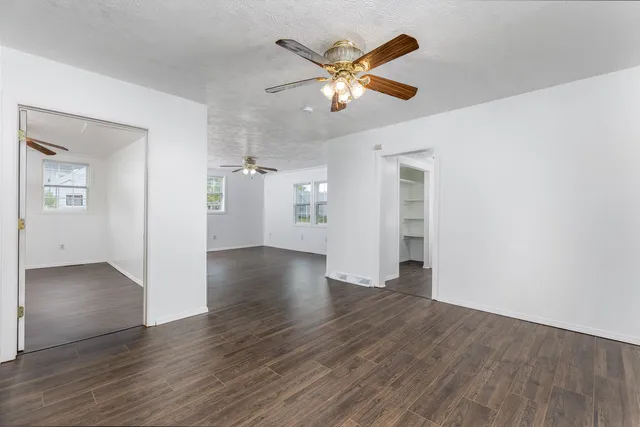an empty room with wooden floor chandelier fan and windows