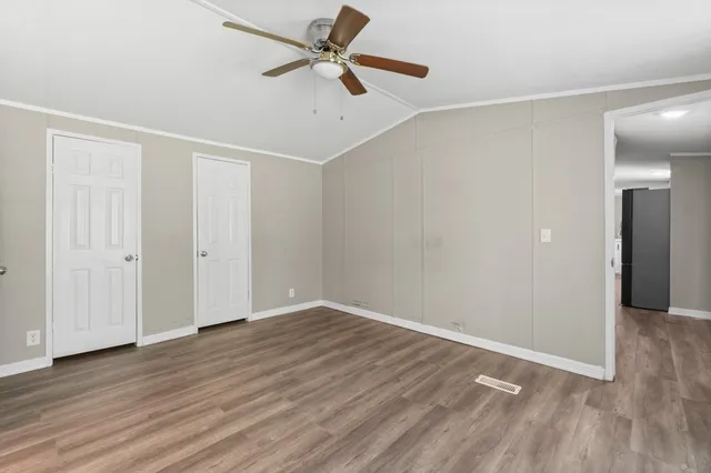 an empty room with wooden floor fan and windows