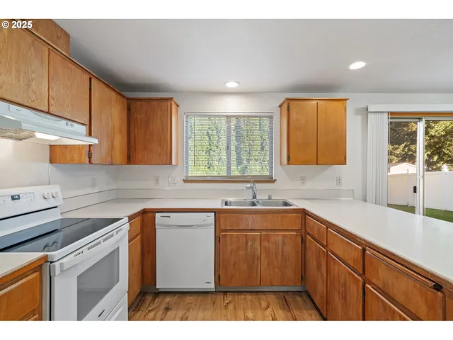 a kitchen with a sink dishwasher a stove and white cabinets with wooden floor