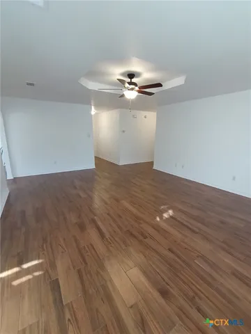 a view of an empty room with chandelier fan and wooden floor
