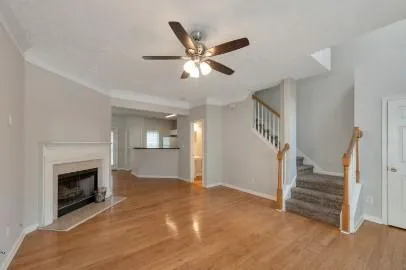 a view of an empty room with wooden floor a ceiling fan and a fireplace
