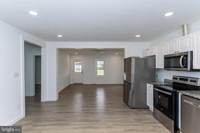 an empty room with wooden floor a ceiling fan and windows