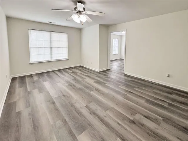 an empty room with wooden floor chandelier fan and windows