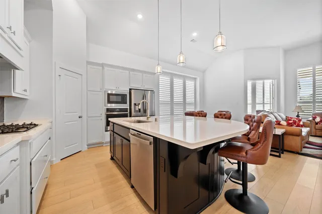 a kitchen with stainless steel appliances kitchen island granite countertop a sink a stove a refrigerator and white cabinets with wooden floor