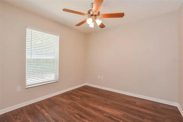 an empty room with wooden floor chandelier fan and windows