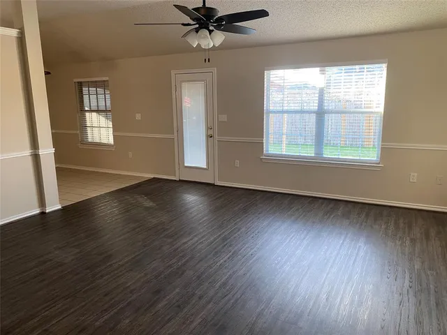 an empty room with wooden floor chandelier fan and windows