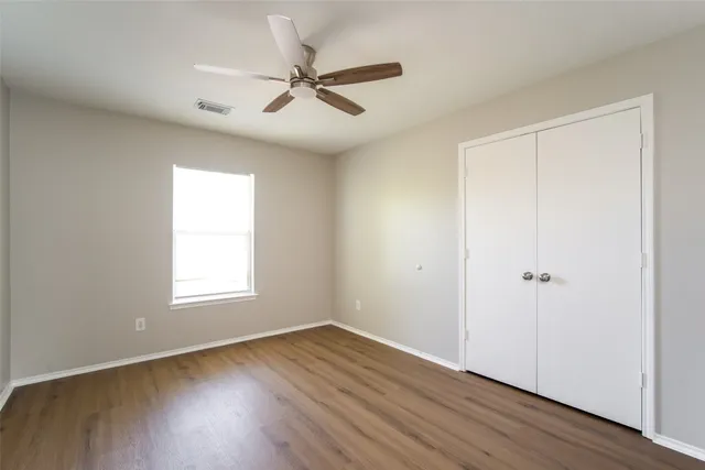 an empty room with wooden floor closet and windows