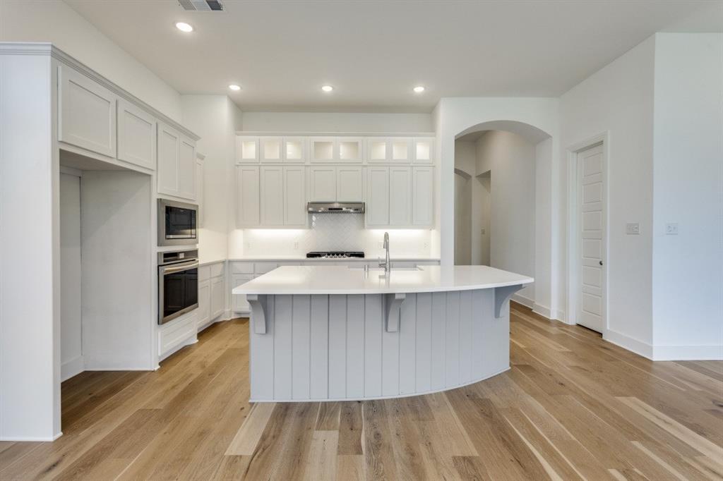 1704 Hydrangea Lane Prosper, TX 75078 - Photo 10 of 25 Kitchen featuring white cabinets, a breakfast bar, decorative backsplash, recessed lighting, and an island with sink