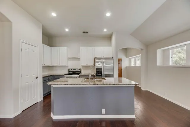 a view of a kitchen with stainless steel appliances granite countertop a stove a sink a refrigerator white cabinets and wooden floor