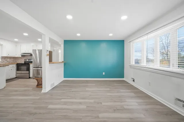 a view of an empty room with wooden floor and a kitchen