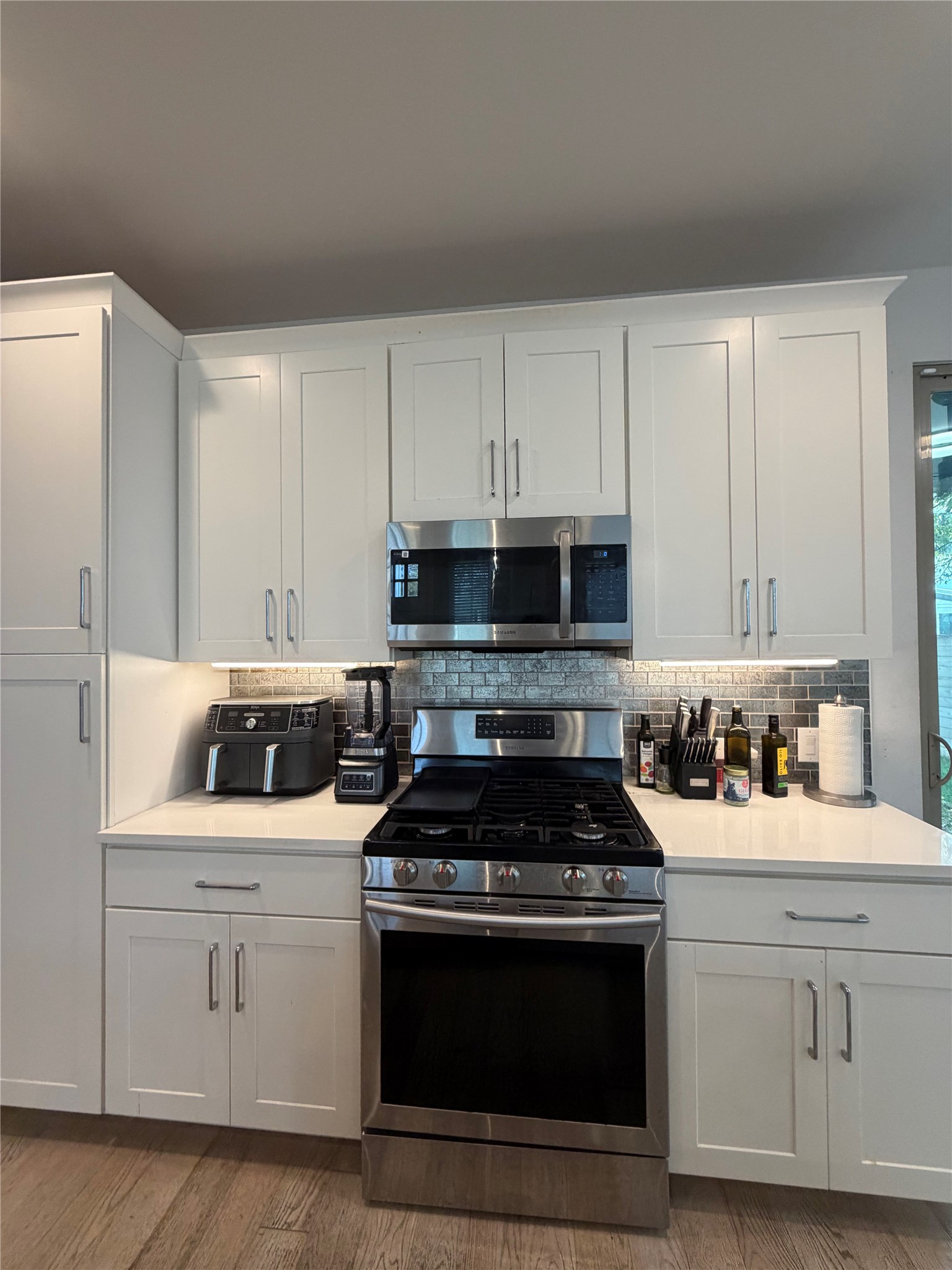 1159 Webberville Road, Unit A Austin, TX 78721 - Photo 11 of 26 Kitchen featuring stainless steel appliances, white cabinets, dark wood-style floors, backsplash, and light stone countertops