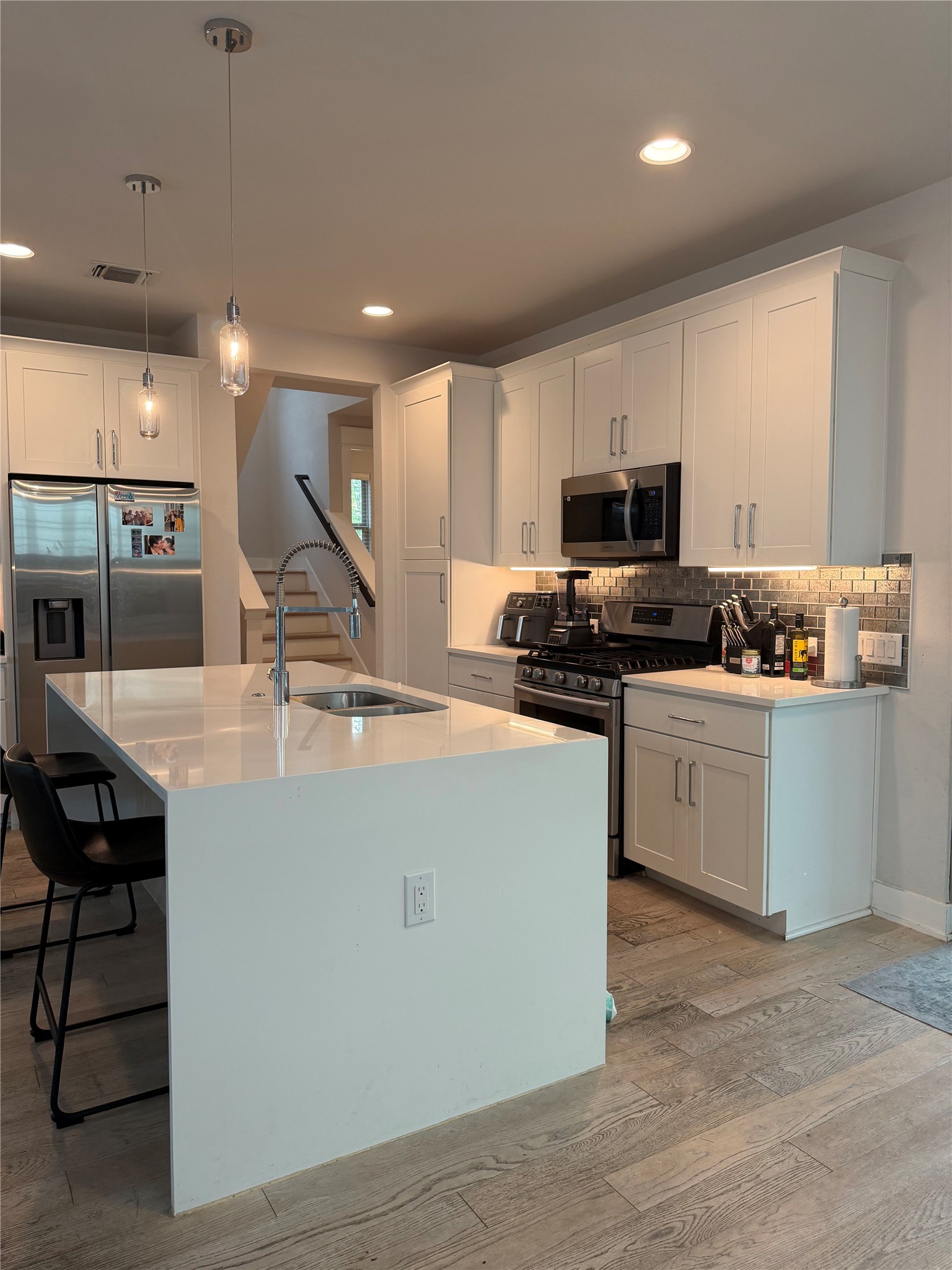 1159 Webberville Road, Unit A Austin, TX 78721 - Photo 9 of 26 Kitchen featuring stainless steel appliances, hanging light fixtures, light stone counters, an island with sink, and white cabinets