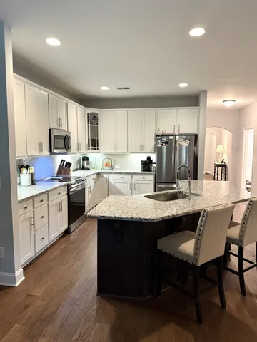 a kitchen with stainless steel appliances granite countertop a sink a stove a refrigerator and white cabinets with wooden floor