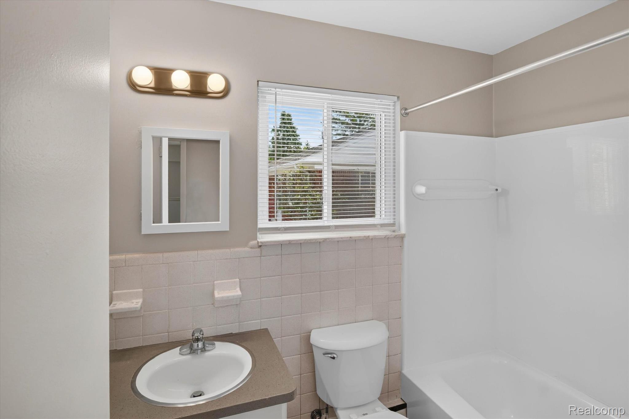 22000 Beck Road, Unit 101 Northville, MI 48167 - Photo 14 of 20 Bathroom featuring a vanity with an integrated sink, a window with blinds, a wall-mounted medicine cabinet, a bathtub with a shower rod, and tiled walls