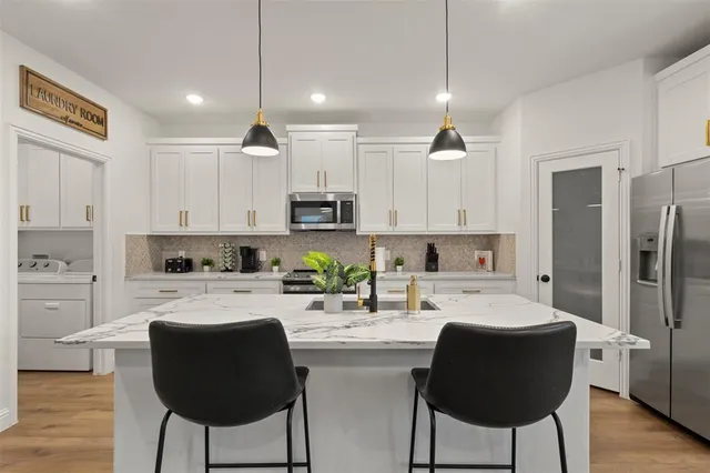 a kitchen with stainless steel appliances kitchen island granite countertop a refrigerator a stove a sink and white cabinets with wooden floor