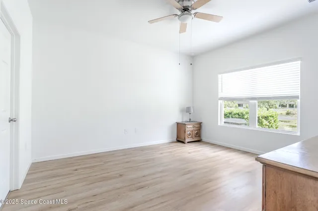 an empty room with wooden floor chandelier fan and windows