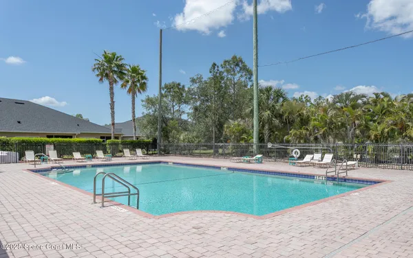 a view of a swimming pool with lawn chairs under an umbrella and palm trees
