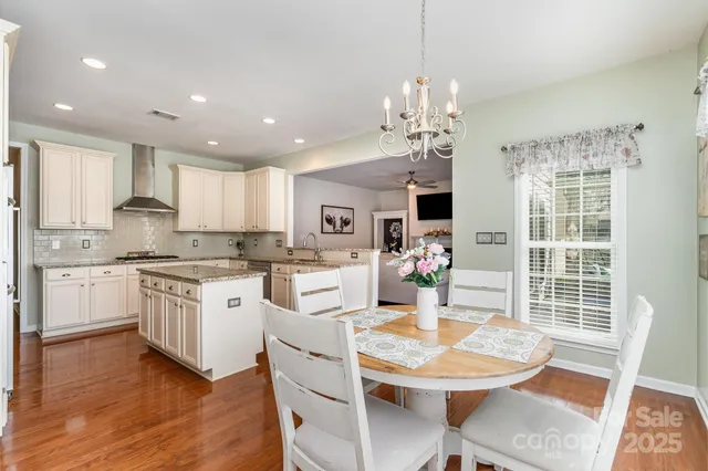 a kitchen with stainless steel appliances kitchen island granite countertop a dining table chairs and white cabinets