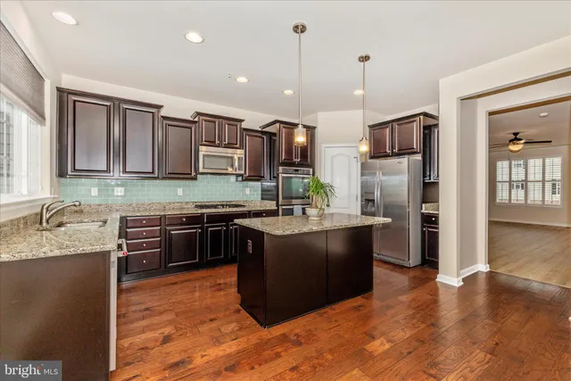 a kitchen with stainless steel appliances granite countertop a sink a refrigerator and a wooden floor